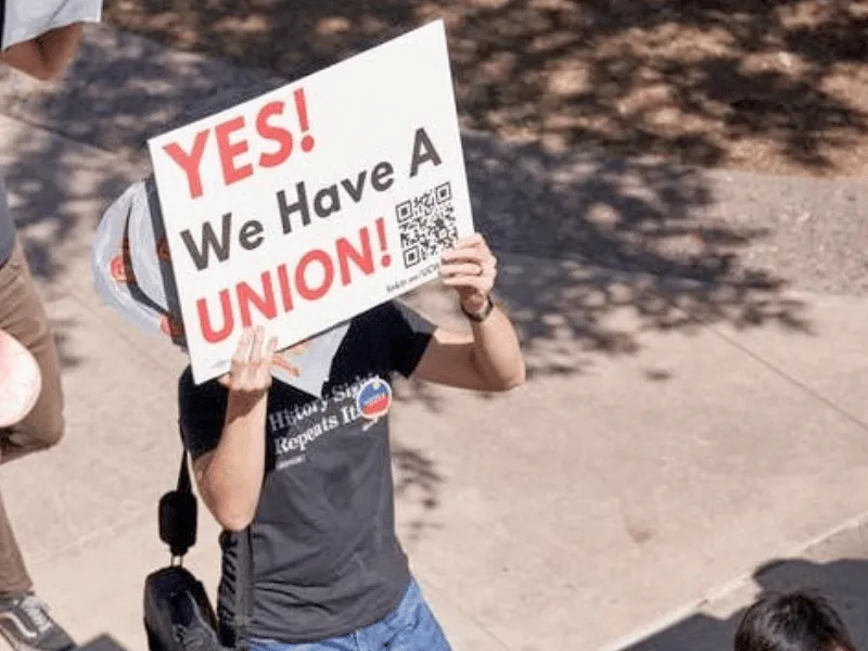 person holding a sign reading "yes! we have a union!"