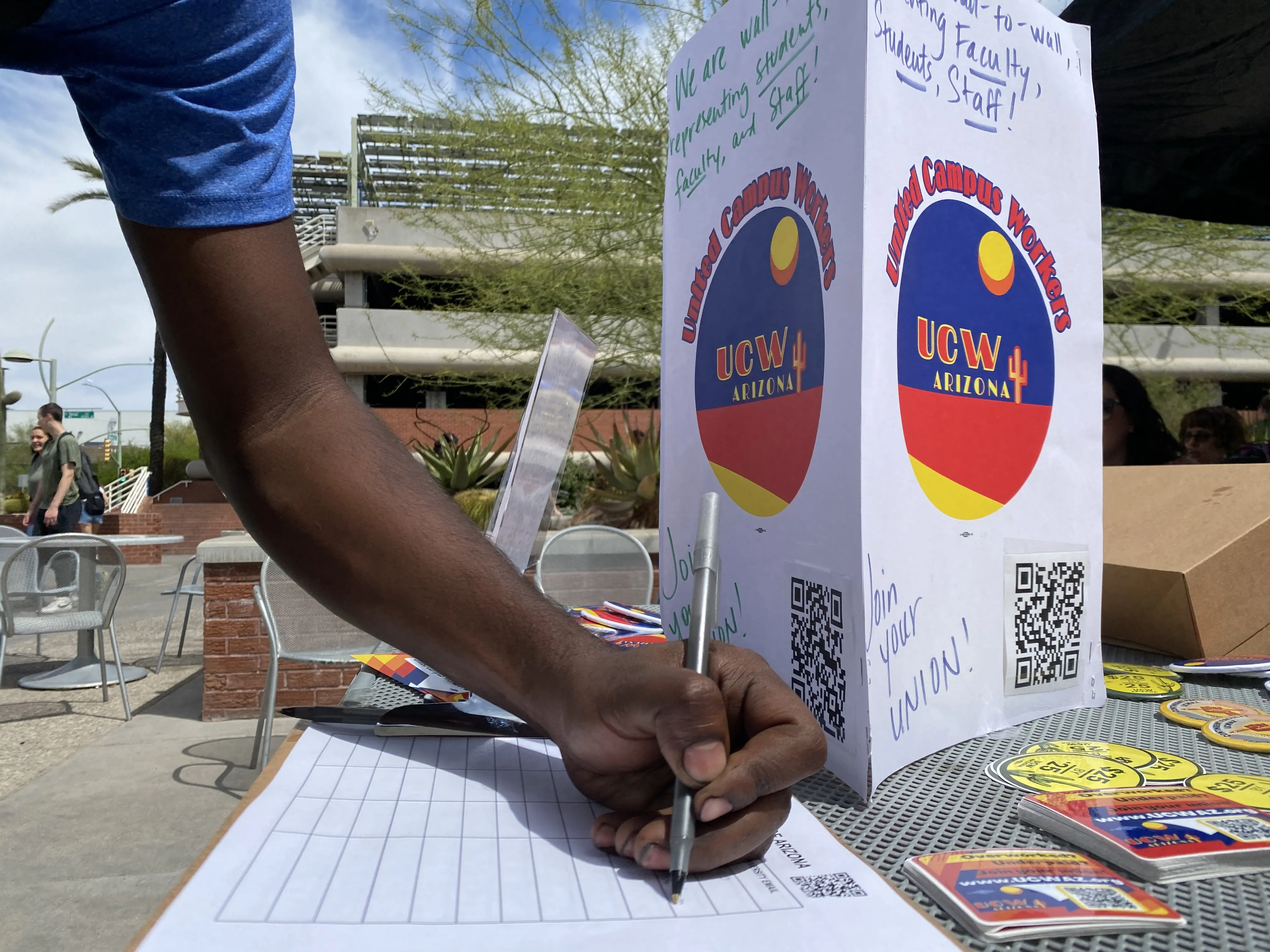 Person signing a clipboard underneath a "join your union" UCWAZ branded sign