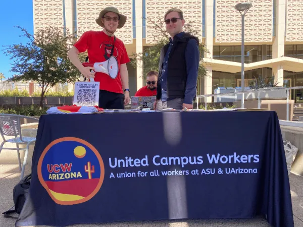 Two people, standing behind a branded UCWAZ table, smiling