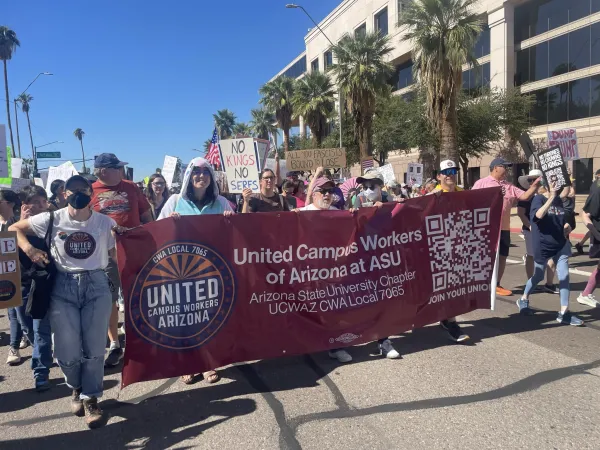 Group of people marching on a sunny day, holding a large red banner that reads "United Campus Workers of Arizona, ASU Chapter"